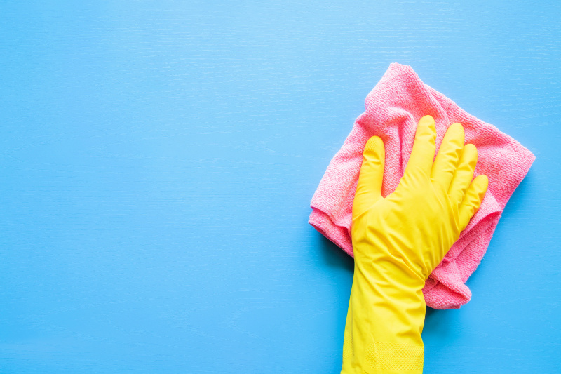 Mano en guante de goma amarillo con un paño rosa para hacer la rutina de limpieza diaria